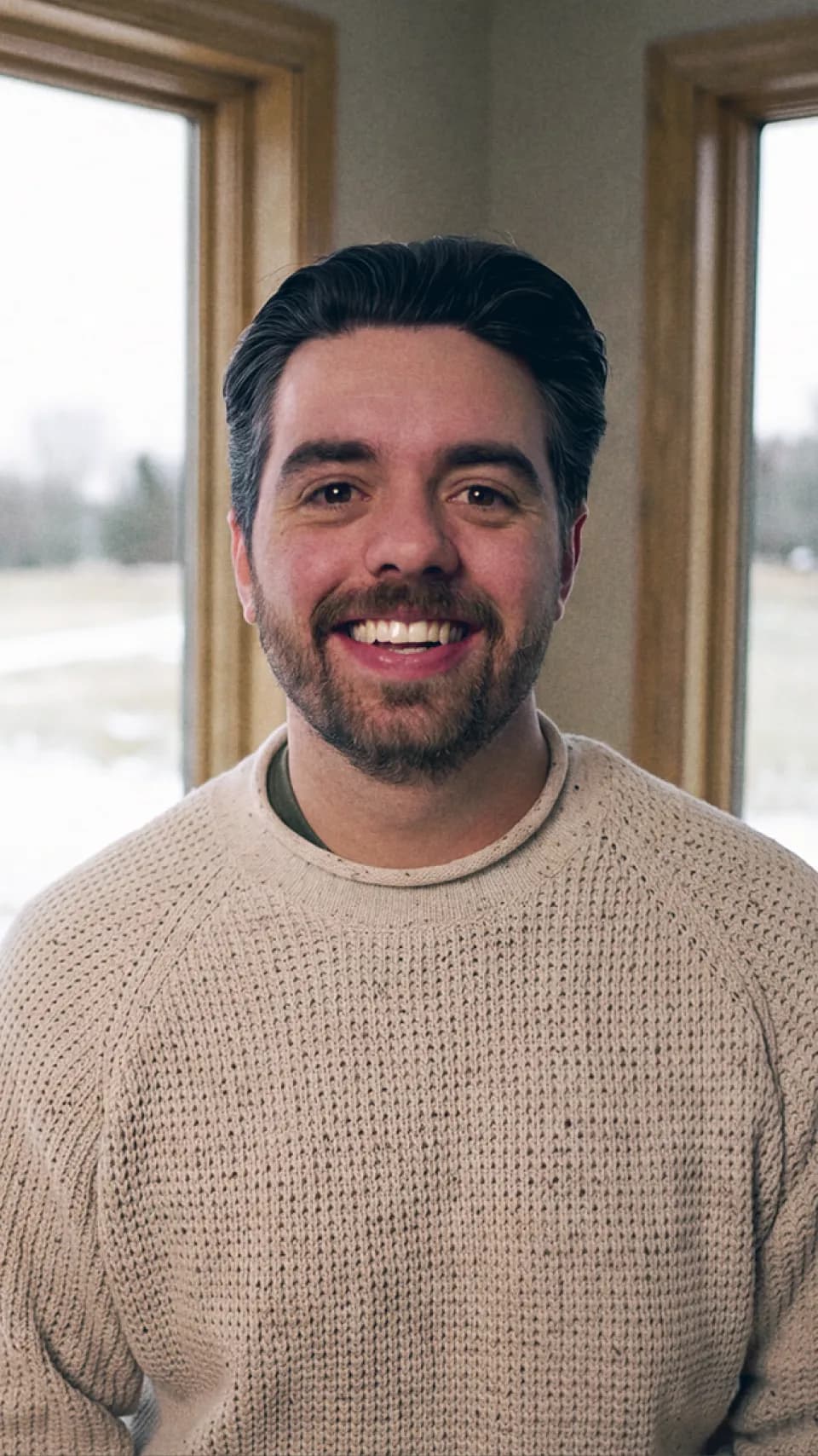 Kyle Sundman in a knit sweater, smiling in a corner room with windows onto a snowy field