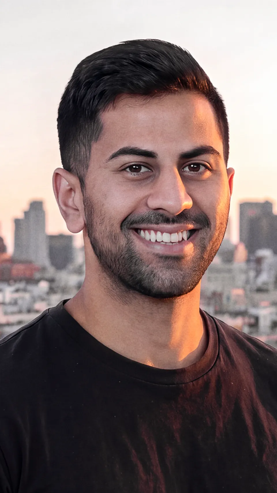Sahil Patel in a black t-shirt, smiling in front of a city skyline at dusk