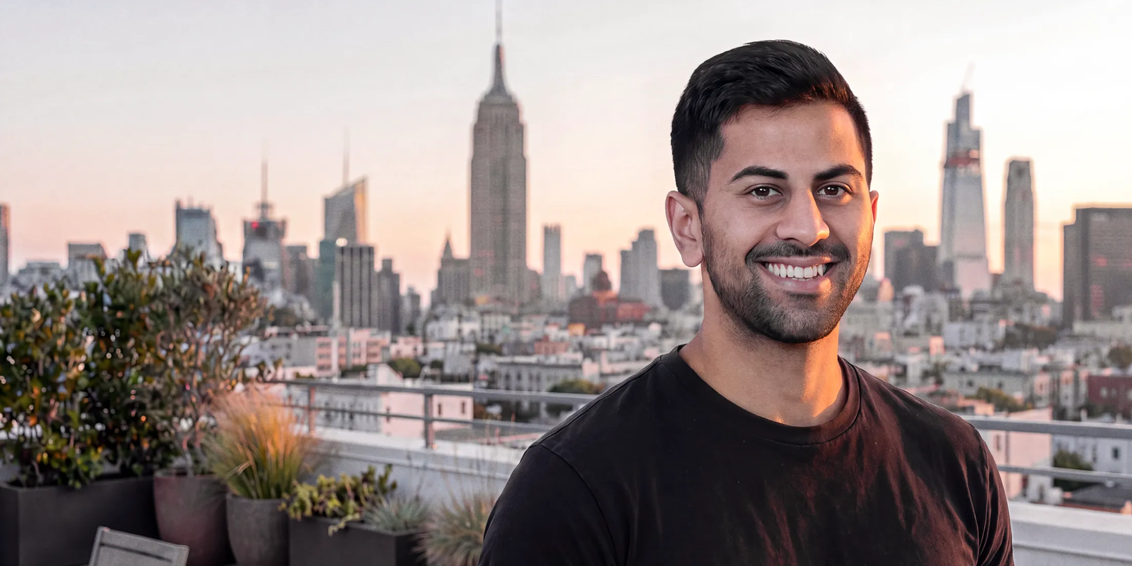 Sahil Patel in a black t-shirt, smiling in front of a city skyline at dusk